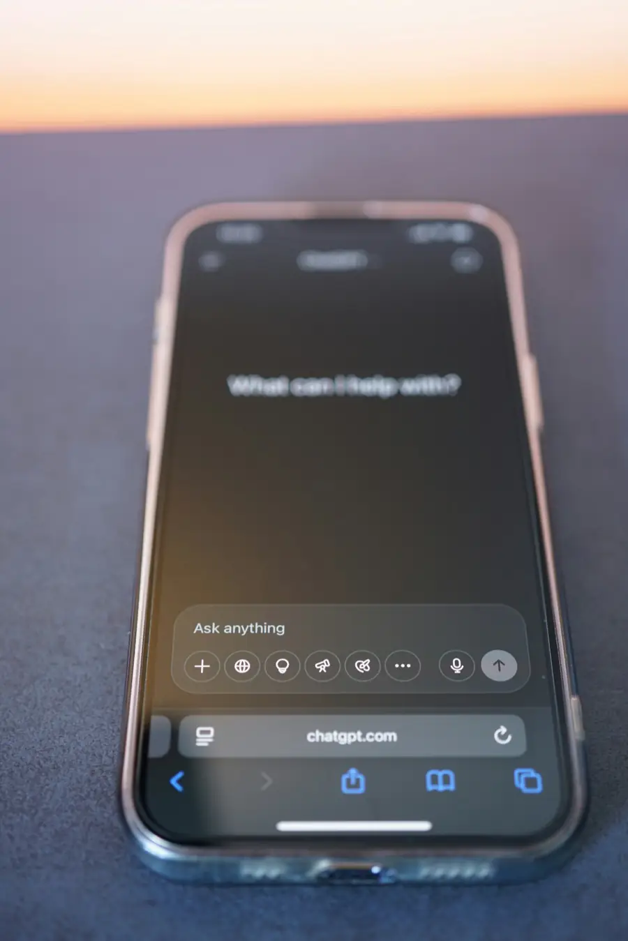 Un telefon așezat pe o masă, cu chatgpt.com deschis în browser și întrebarea „What can I help with?” pe ecran.